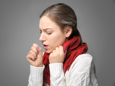 Young woman in warm scarf coughing on gray backgroundの写真素材