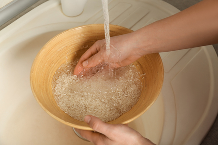 Woman rinsing rice in bowl under running waterの写真素材