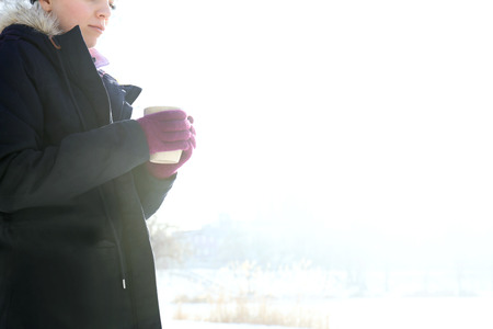 Female hands in cute pink gloves holding cup on winter background