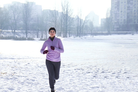 Sportive young woman running in winter parkの写真素材