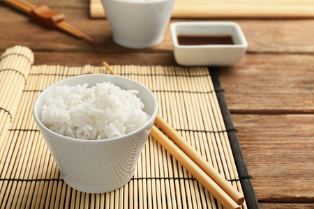 Bowl of rice and chopsticks on bamboo matの写真素材