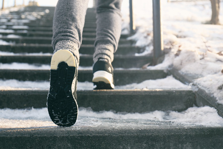 Legs of sportive woman running up stairs in winter, close up view
