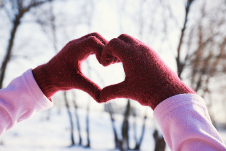 Female hands in shape of love heart on winter backgroundの写真素材