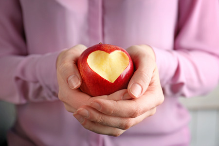 Woman hands holding fresh red apple with heart-shaped cut out, closeupの写真素材
