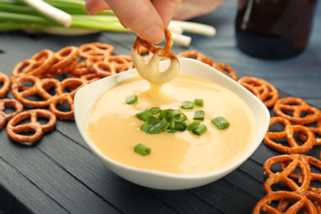 Female hand dipping pretzel in bowl with beer cheese dip, closeupの写真素材