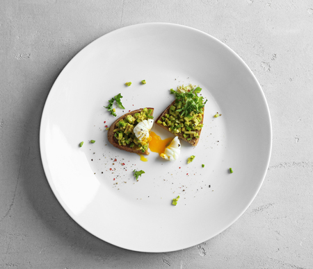 Toast with poached egg and chopped avocado on plateの写真素材