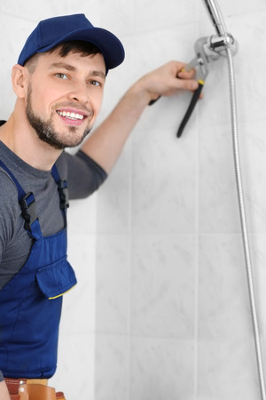 Plumber repairing shower head in bathroomの写真素材