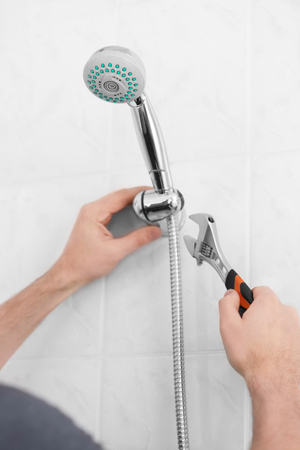 Plumber repairing shower head in bathroomの写真素材