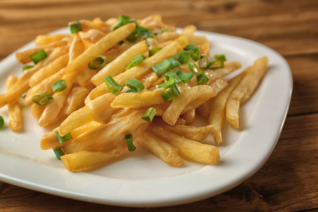 Plate with cheese fries and chopped green onion on wooden table