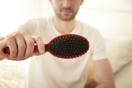 Hair loss concept. Young man with hair comb, closeup