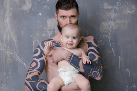 Handsome tattooed young man holding cute little baby on gray backgroundの写真素材