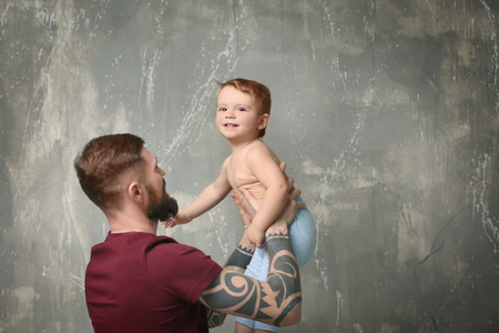 Handsome tattooed young man holding cute little boy on gray backgroundの写真素材