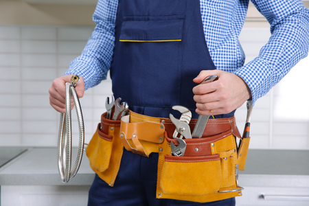 Plumber in blue uniform with tool belt at kitchen, closeupの写真素材