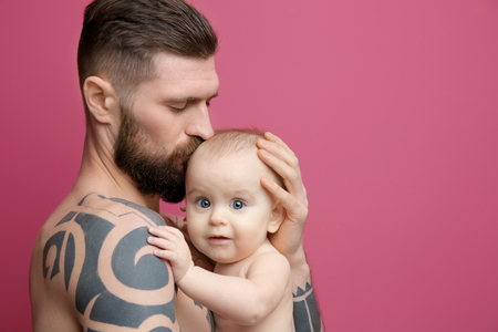 Handsome tattooed young man holding cute little baby on color backgroundの写真素材