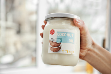 Female hand holding jar with coconut oil on blurred backgroundの写真素材