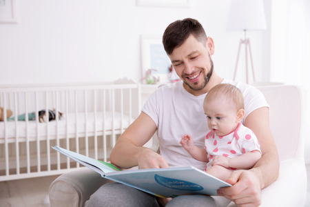 Father showing book to cute baby daughter  at homeの写真素材