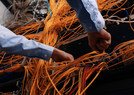 Hands of young engineer connecting cables in server room