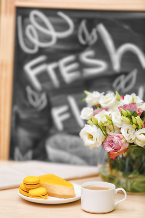 Cup of coffee, tasty cake and beautiful bouquet of flowers on table in cafeの写真素材