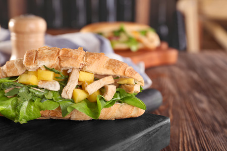 Wooden board with chicken salad in croissant bun on tableの写真素材
