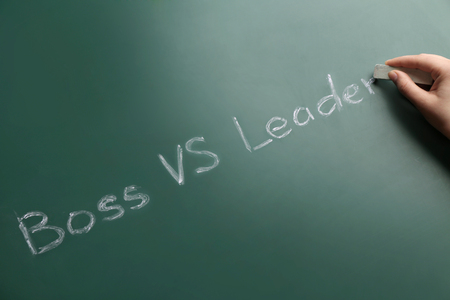 Female hand with chalk and words BOSS VS LEADER on chalkboardの写真素材