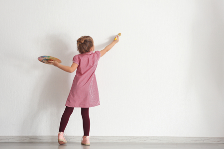 Cute little girl painting on wall in empty roomの写真素材
