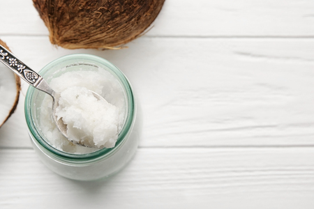 Spoon with fresh coconut oil and glass jar on white wooden backgroundの写真素材