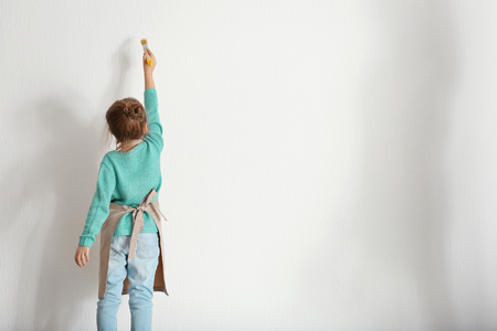 Cute little girl painting on light wallの写真素材