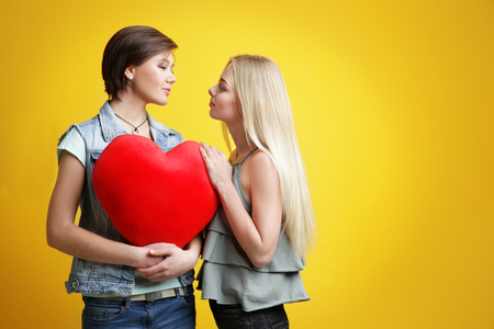 Young lesbian couple with decorative heart on color backgroundの写真素材
