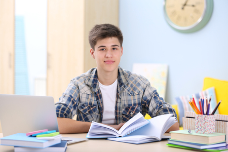 Teenager sitting at table and studying at homeの写真素材