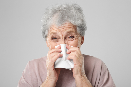 Portrait of elderly woman sneezing in handkerchief on grey backgroundの写真素材