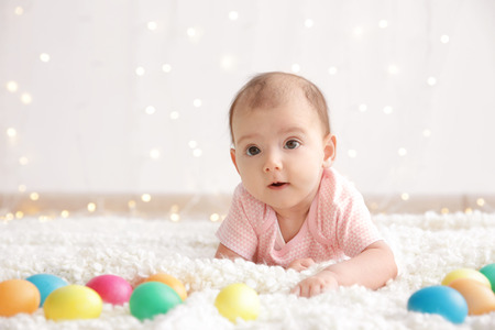 Cute little baby with colorful Easter eggs lying on plaid at homeの写真素材