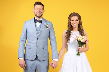 Happy wedding couple holding hands on color backgroundの写真素材