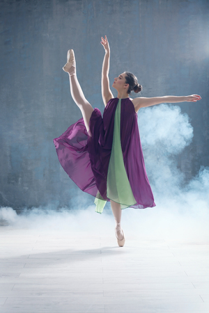 Young beautiful ballerina dancing in studio with smoke effectの写真素材