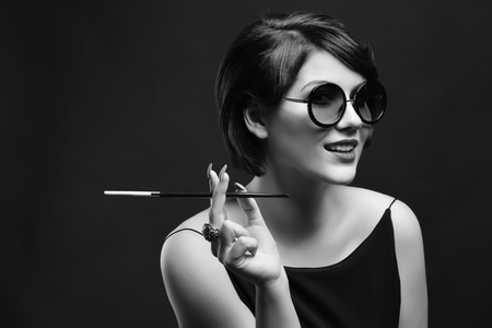Young woman with cigarette holder on dark backgroundの写真素材