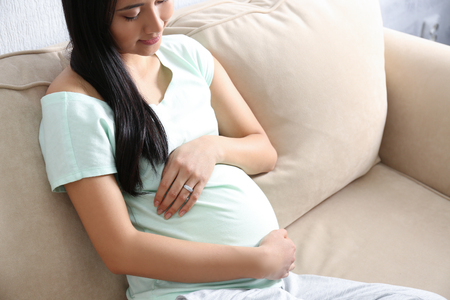 Pregnant Asian woman sitting on sofa at homeの写真素材