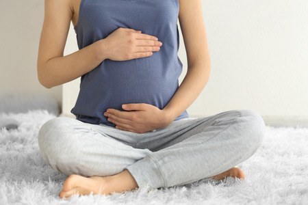Beautiful pregnant woman sitting on floor at homeの写真素材