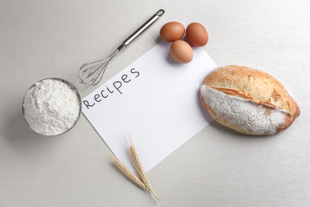 Sheet of paper with text RECIPES and bread on light backgroundの写真素材