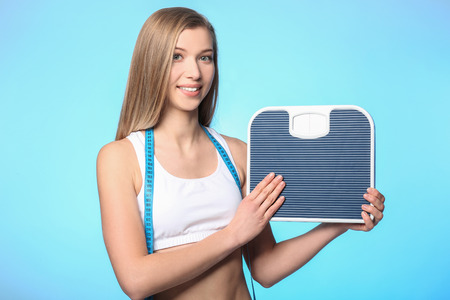 Diet concept. Young beautiful woman holding floor scales on light backgroundの写真素材