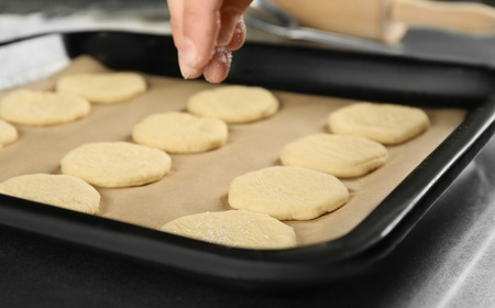 Female hand pouring sugar on cookies dough, closeupの写真素材