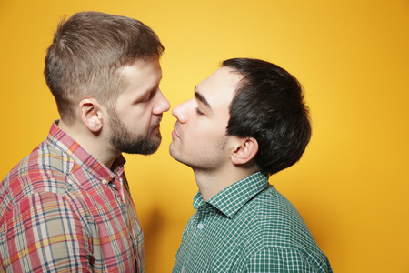 Happy gay couple posing on yellow backgroundの写真素材