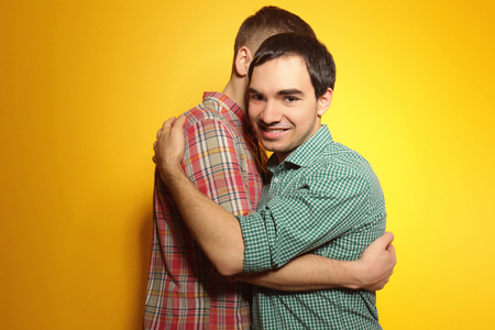 Happy gay couple posing on yellow backgroundの写真素材
