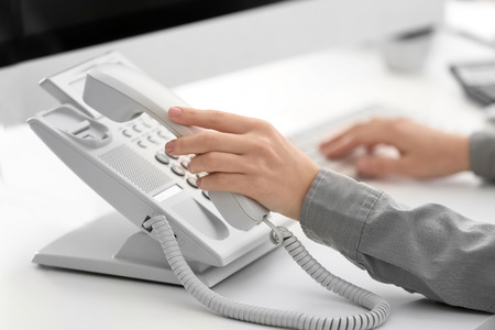 Woman picking up telephone receiver in officeの写真素材