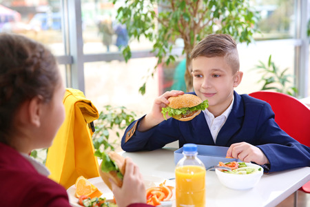 Children sitting at cafeteria table while eating lunchの写真素材