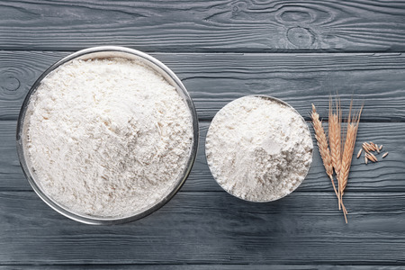 Two bowls of white flour and wheat ears on wooden backgroundの写真素材