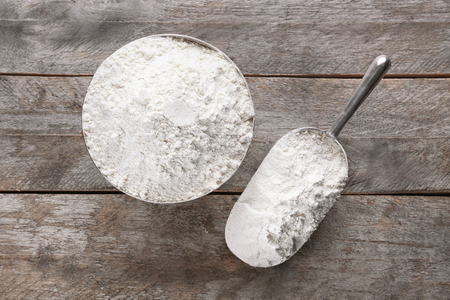 Metal bowl and scoop full of white flour on grey wooden backgroundの写真素材