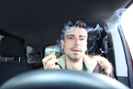 Young man driving a car and smoking cigaretteの写真素材