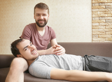 Happy gay couple resting on sofa at homeの写真素材