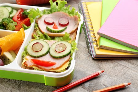 Funny sandwiches in lunch box and colorful stationery on wooden backgroundの写真素材