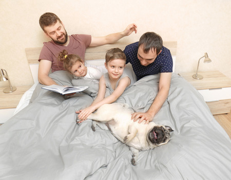 Male gay couple with children resting in bed at homeの写真素材