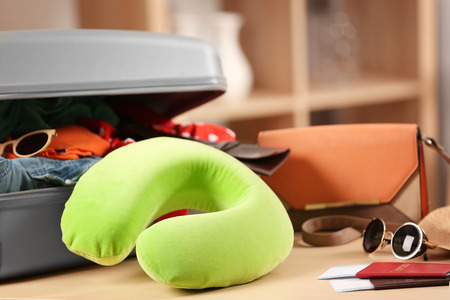 Travel pillow and suitcase with different things on wooden tableの写真素材